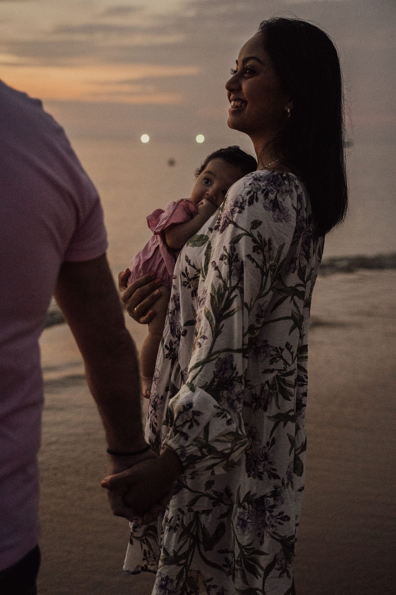 A mother holding her baby gently on the beach at sunset