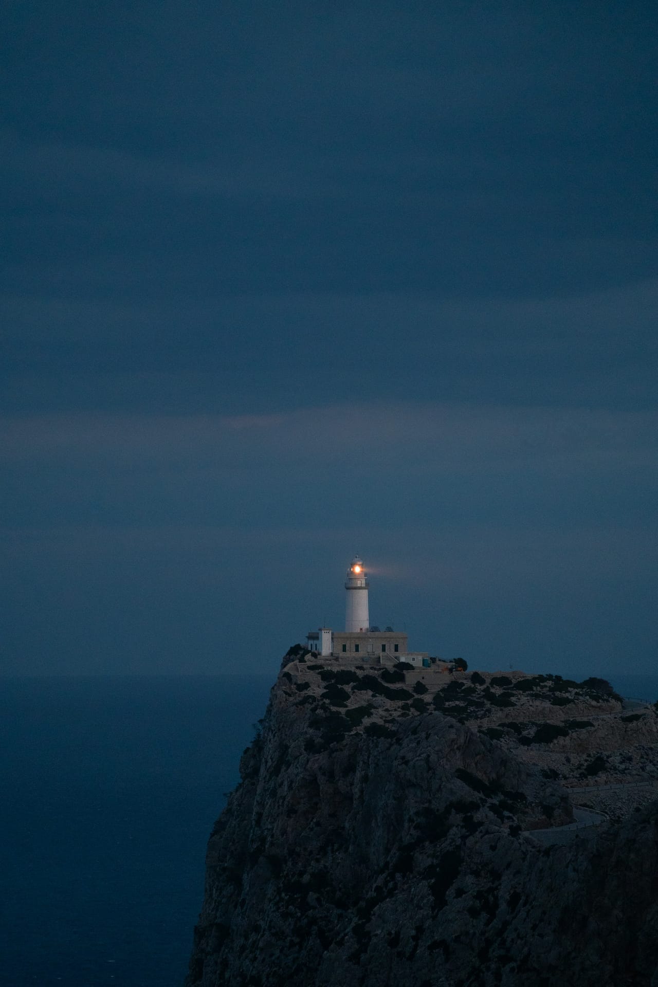 Guiding light from a coastal lighthouse against a dusk ocean